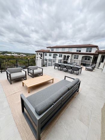 A patio with a couch, chairs, and a table with a view of a house and hills.